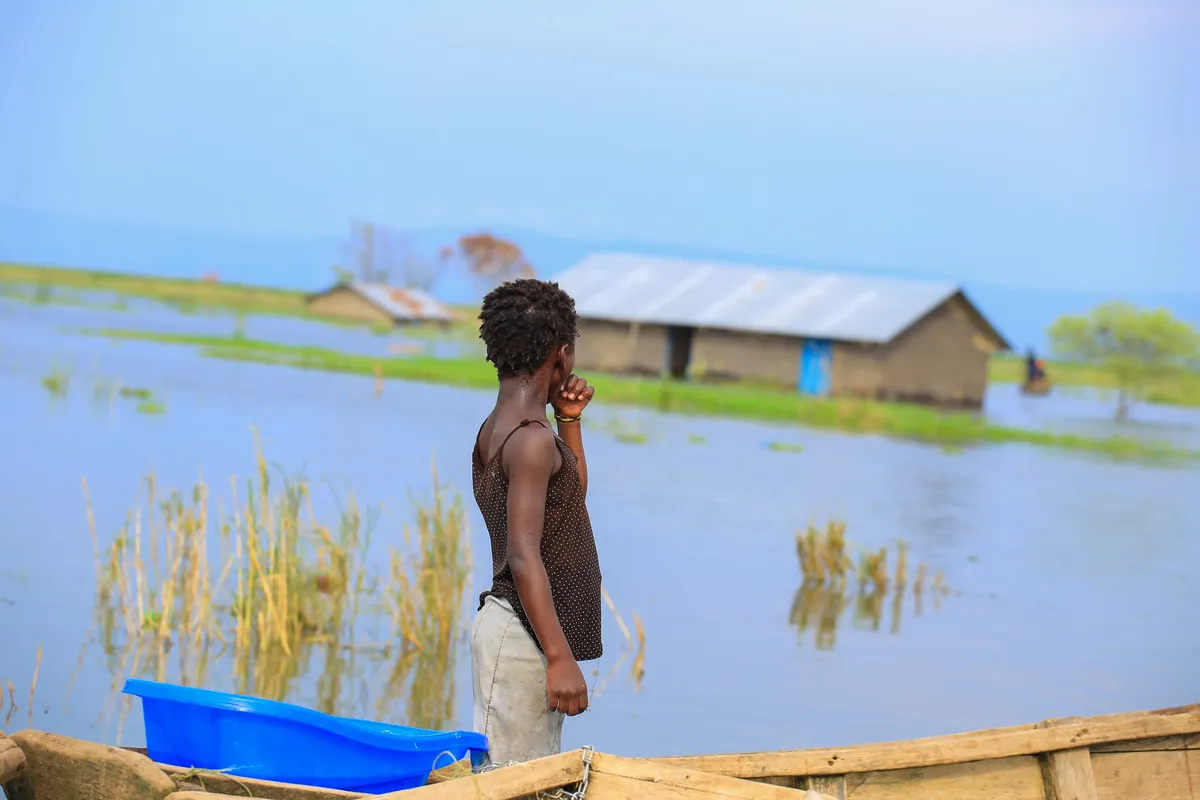 Woman standing in a dugout canoe amid floodwaters that have submerged her village — the human face of climate displacement